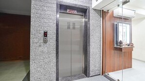 An elevator with a digital control panel, a sign above it, and a reception desk with a mirror. - Fabhotel Vishala Inn (Ahmedabad)