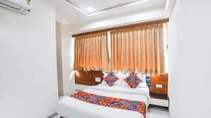 A hotel room with a large bed, a wooden headboard, and a window with curtains. - Fabhotel Vishala Inn (Ahmedabad)