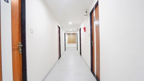 A long, narrow hallway with doors on both sides, a light switch, and a fire alarm on the right wall. - Fabhotel Vishala Inn (Ahmedabad)