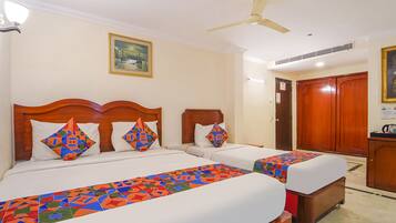 A hotel room with two beds, a ceiling fan, a painting on the wall, and a wooden wardrobe.
