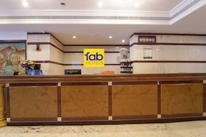 A reception area with a marble counter, a 'fab hotels' sign, a clock, and a fan. - Fabhotel Seven Olives (Bengaluru)
