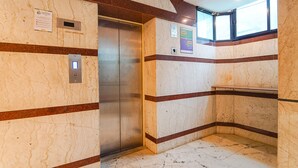 An elevator with marble walls and a metal door, a sign on the wall, and a window above the door. - Fabhotel Seven Olives (Bengaluru)