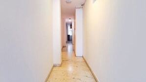 A narrow hallway with white walls and a marble floor, leading to a room with a window and a door. - Fabhotel Seven Olives (Bengaluru)