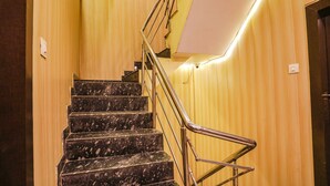 A staircase with marble steps and metal railings, leading to a landing with a light switch and a door. - Fabhotel Bala Ji Inn (Varanasi)