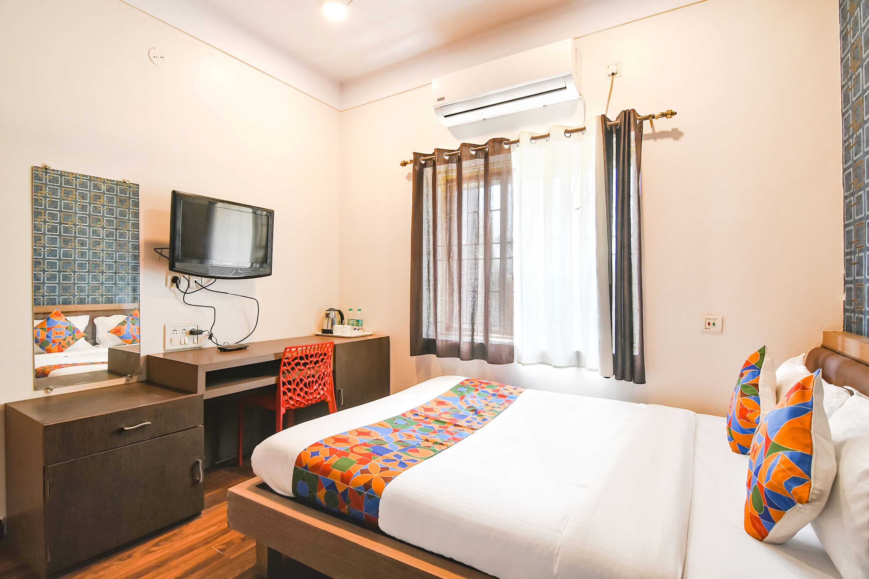 Une chambre d’hôtel avec un lit, un bureau avec une télévision, un climatiseur et une fenêtre avec des rideaux.