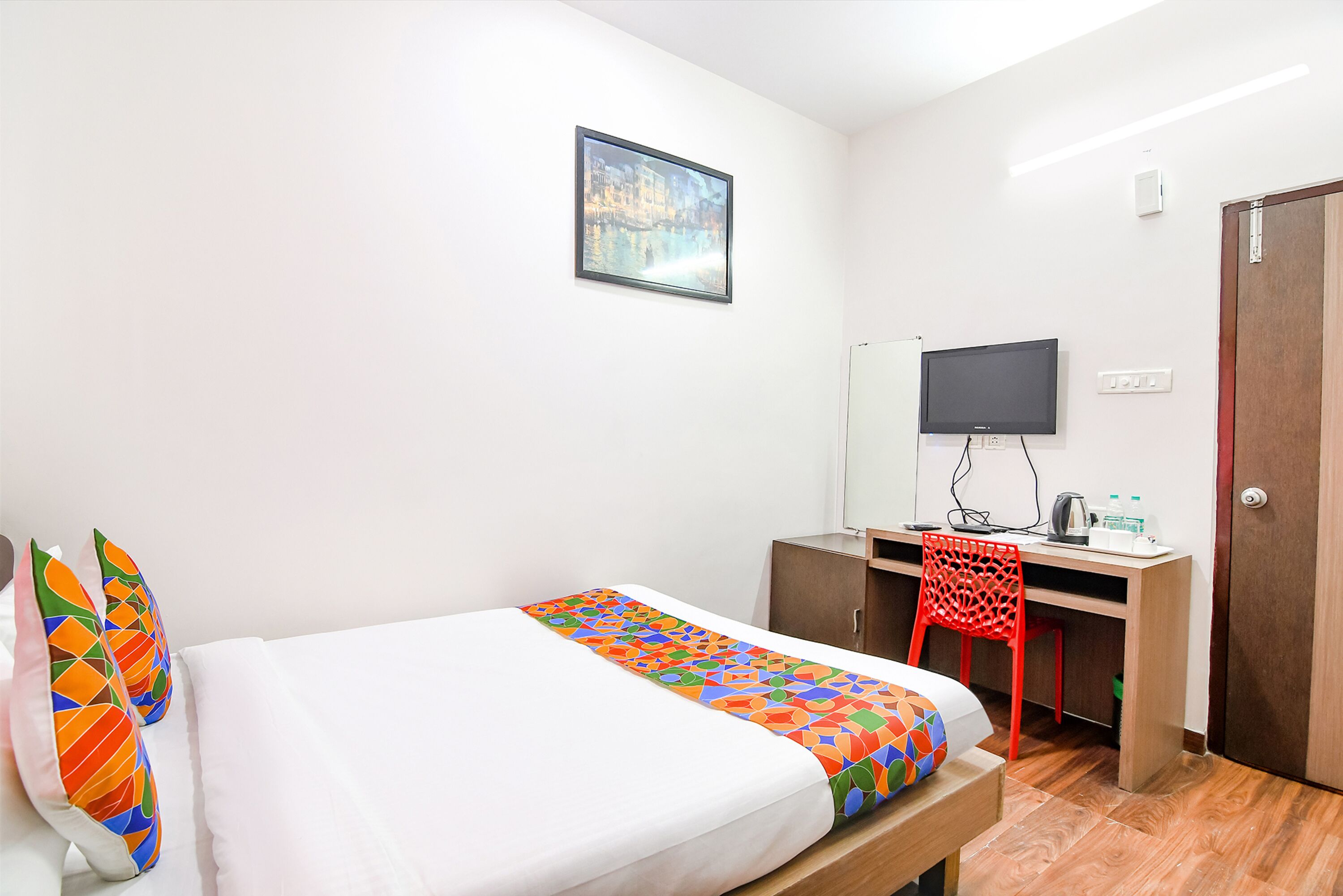 A hotel room with a bed, a desk, a chair, a television, and a door.