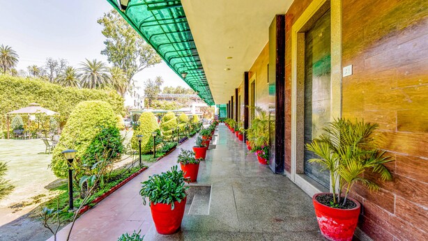 A covered corridor with potted plants, a tiled floor, and a view of a landscaped area with trees and a building in the background. - Fabhotel Resort Royal Garden Retreat (Abu Road)