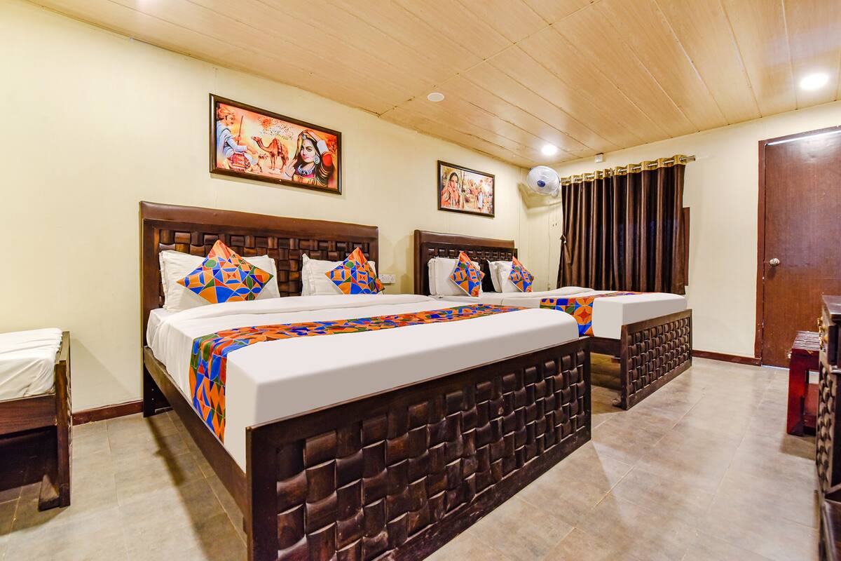 A hotel room with two beds, a wooden headboard, a ceiling fan, and two framed pictures on the wall.