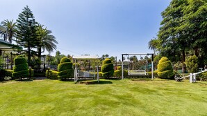 A well-maintained garden with neatly trimmed hedges, a gazebo, and a swing set. - Fabhotel Resort Royal Garden Retreat (Abu Road)