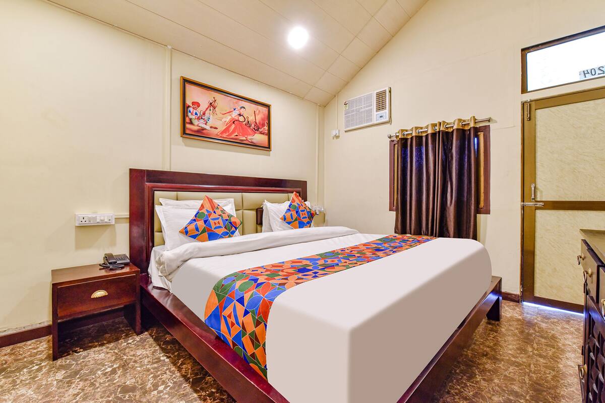 A hotel room with a large bed, a nightstand with a phone, a painting on the wall, and a curtain.