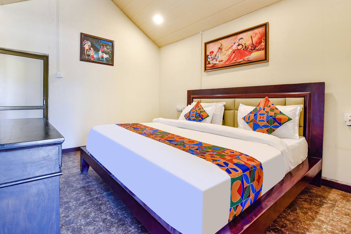A hotel room with a large bed, a wooden headboard, and two paintings on the walls.