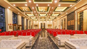 A conference room with rows of red chairs and white sofas, a polished marble floor, and a decorative ceiling with recessed lighting. - Fabhotel Saalt Bandhan Resort (Pashchimi Muzaffarpur)