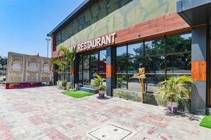 A restaurant with a modern facade, large windows, and potted plants in the entrance area. - Fabhotel Saalt Bandhan Resort (Pashchimi Muzaffarpur)
