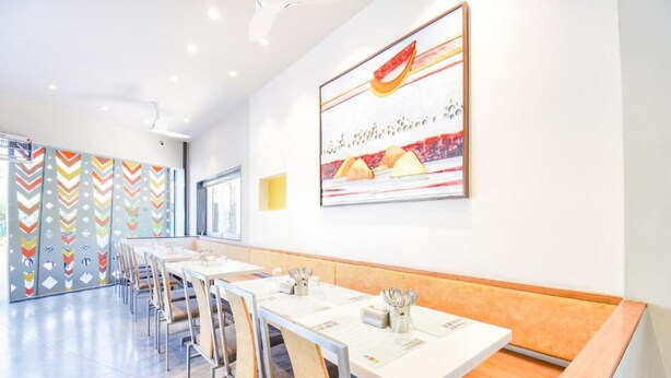 Un espace de restauration moderne avec de longues tables et des bancs, un motif mural aux couleurs vives et un grand tableau abstrait.