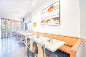 A modern dining area with long tables and benches, a colorful wall pattern, and a large abstract painting. - Fabhotel Ananta Sagar (Pune)