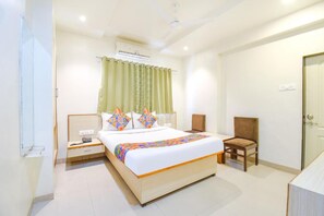 A hotel room with a bed, a chair, a nightstand, an air conditioning unit, and a door.
