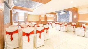 Une salle de banquet avec des rangées de tables et de chaises, chacune recouverte d’une nappe blanche et ornée d’un ruban rouge.
