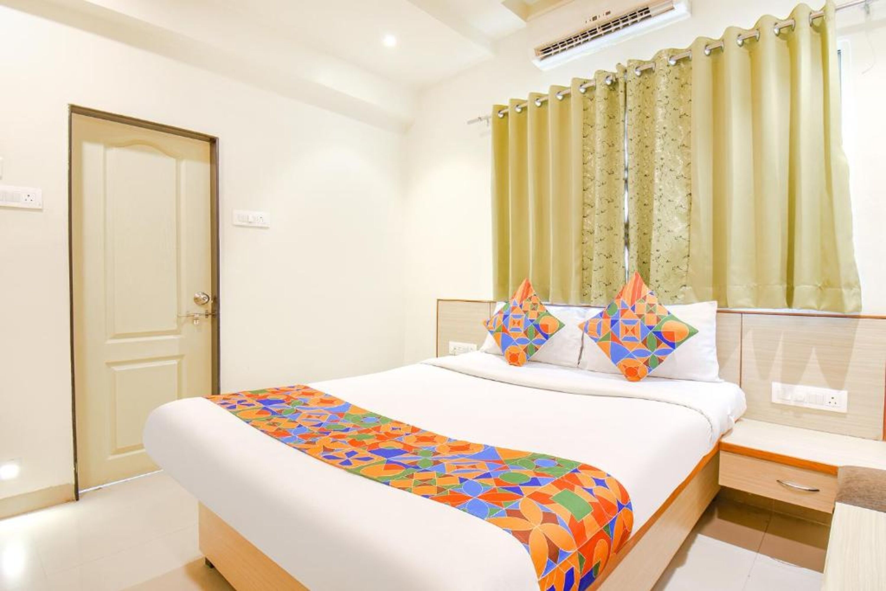 A hotel room with a bed, a bedside table, a nightstand, and a window with curtains.