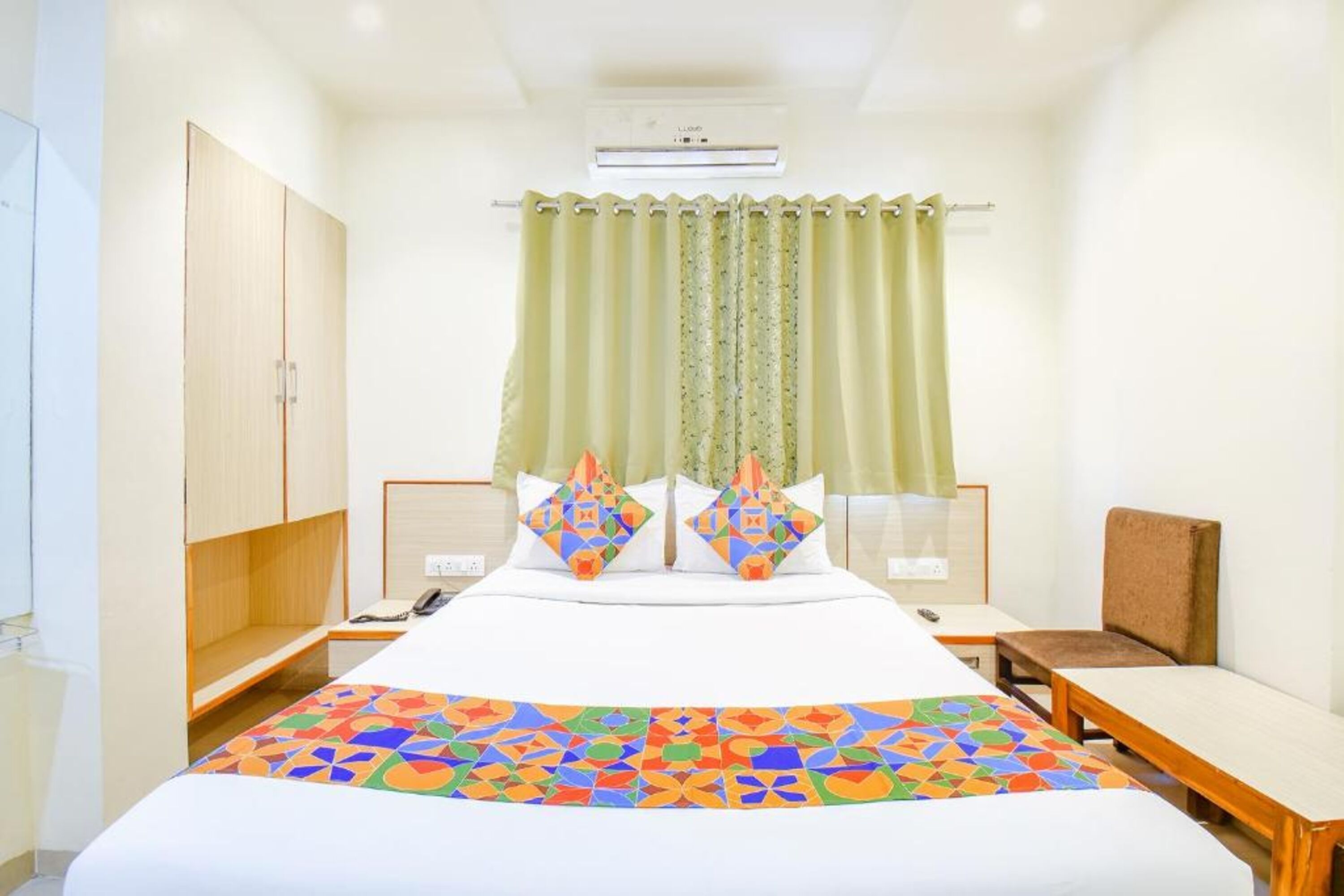 A hotel room with a bed, a desk, a chair, a wardrobe, and a curtain.