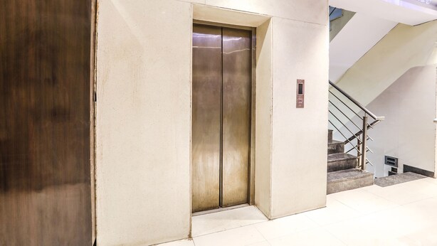 An elevator in a building with a metallic finish, adjacent to a staircase with a glass railing. - Fabhotel Starlight Nx (Chhatrapati Sambhajinagar)