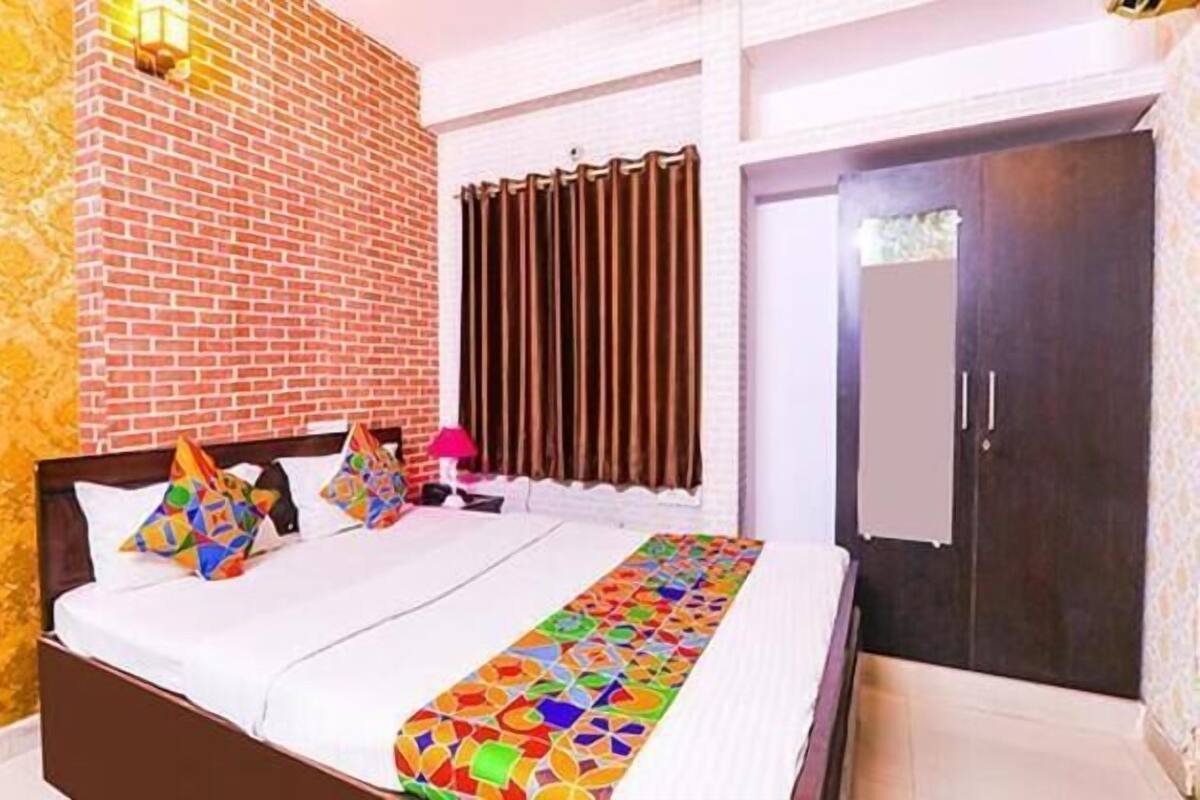 Habitación de hotel con pared de ladrillo, cama con almohadas de colores, ventana con cortinas y una puerta.