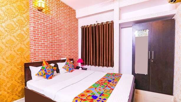 A hotel room with a brick-patterned wall, a bed with a colorful geometric bedspread, a bedside lamp, and a wardrobe. - FabHotel The Hudco Grand (Patna)
