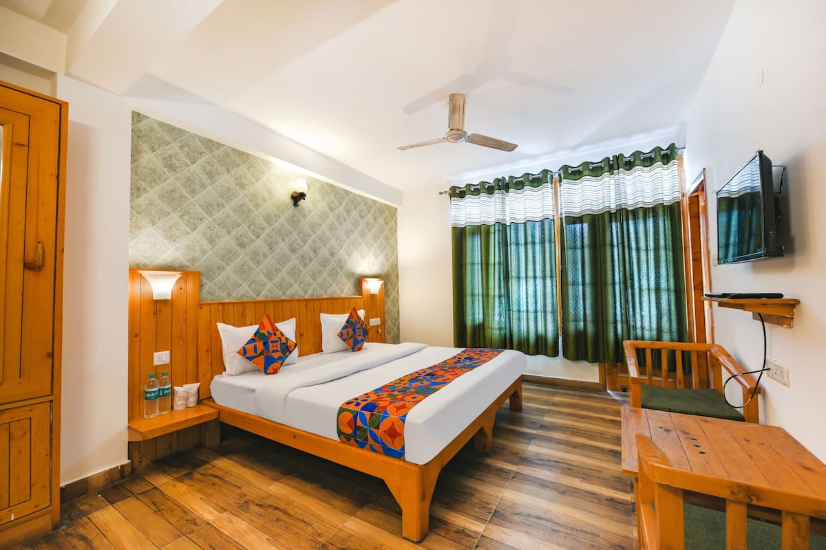 A hotel room with a wooden bed, a wooden desk, a ceiling fan, and a TV mounted on the wall.