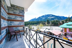 A balcony with a view of a mountain range, a chair, and a building with a green roof. - Fabhotel Kanchnikoot (Manali)