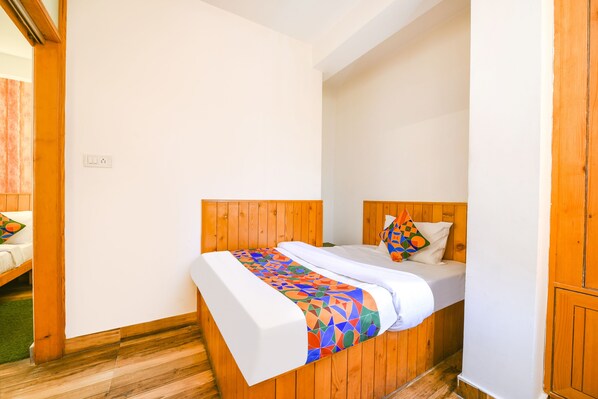 A single bed with a colorful geometric-patterned bedspread, a white pillow, and a wooden headboard in a room with wooden walls and flooring. - Fabhotel Kanchnikoot (Manali)