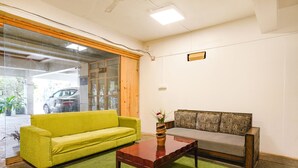 A room with a green sofa, a patterned sofa, a wooden coffee table, and a glass door leading outside. - FabHotel Blue Dawn Suites (Hyderabad)