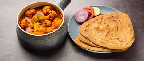Un bol de curry naranja con vegetales y un plato de pan plano sobre una superficie gris.