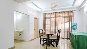 A room with a dining table, chairs, a green tablecloth, a ceiling fan, a window with curtains, and a sink. - FabHotel Blue Dawn Suites (Hyderabad)