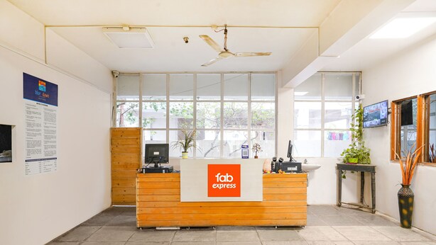A reception area with a wooden desk, a ceiling fan, large windows, and a wall-mounted TV. - FabHotel Blue Dawn Suites (Hyderabad)