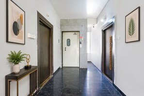 A hallway with a marble floor, framed artwork on the walls, and a potted plant on a console table. - FabHotel Blue Dawn Suites (Hyderabad)