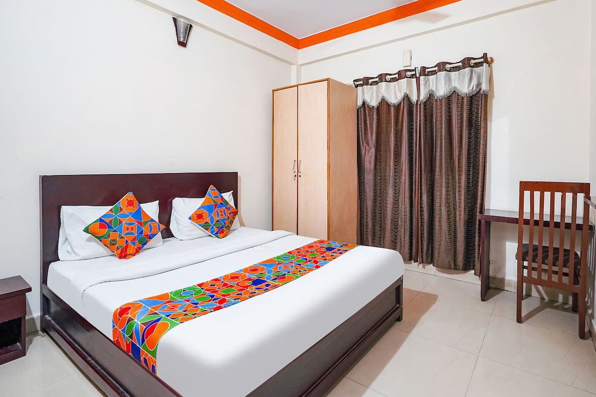 Una cama bien hecha con un edredón colorido, un armario de madera, una silla y una ventana con cortinas.
