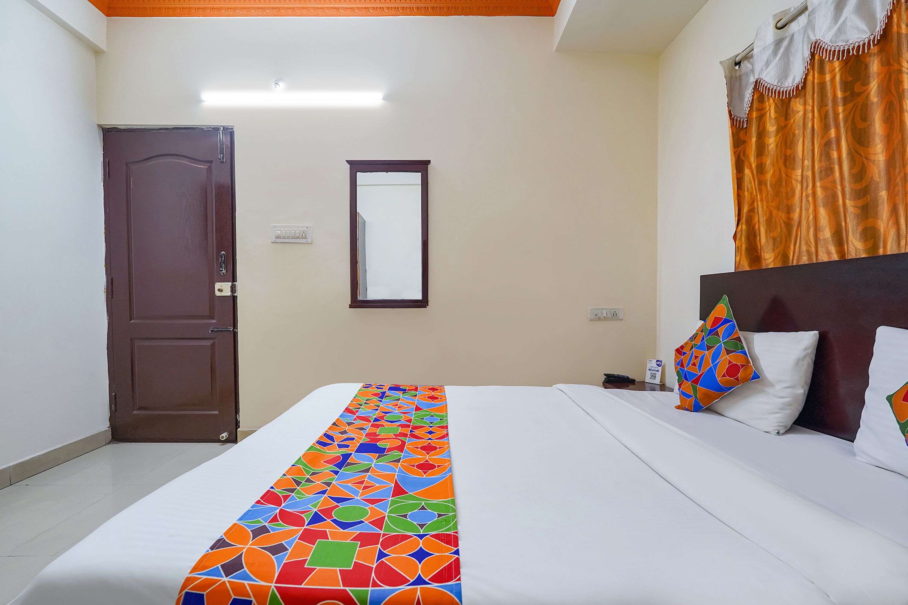 A hotel room with a bed, a door, a mirror, and a curtain.