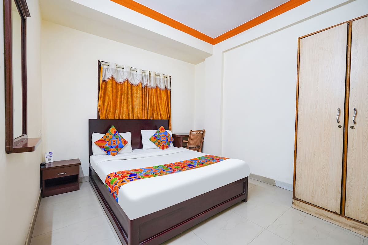 Un dormitorio ordenado con cama, mesita de noche, armario y ventana con cortinas.