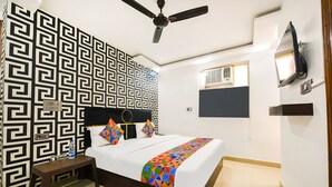 Ein ordentlich eingerichtetes Hotelzimmer mit einem Bett, einem Nachttisch, einem Deckenventilator, einem an der Wand montierten Fernseher und einer Wand mit Muster.