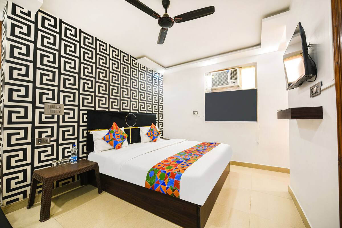 Une chambre d’hôtel bien aménagée, avec un lit, une table de chevet, un ventilateur de plafond, un téléviseur fixé au mur et un papier peint à motifs.