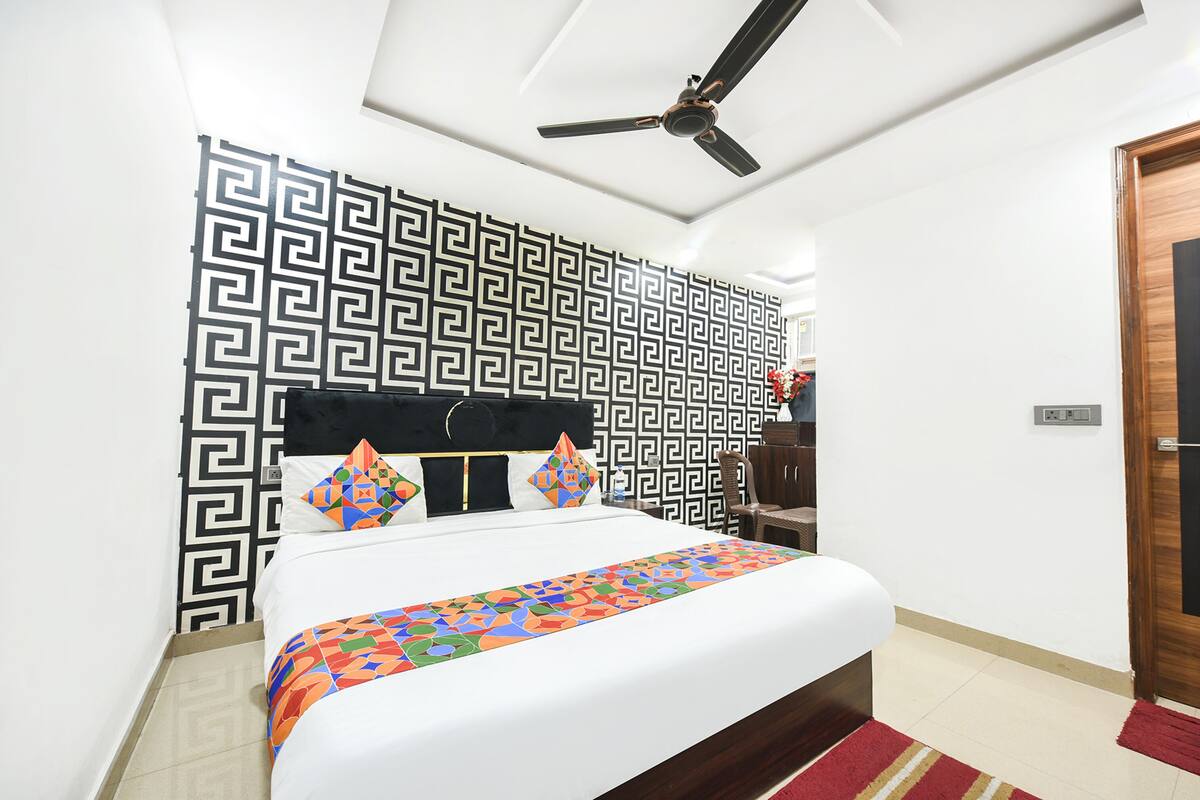 Une chambre d’hôtel bien rangée, avec un lit, un ventilateur de plafond, un mur décoré de motifs et une porte en bois.