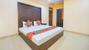 A large bed with a colorful bedspread, a wooden headboard, and two nightstands. - Fabhotel Bns Lodge (Bengaluru)