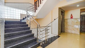 A modern hotel lobby with a marble staircase, a fire extinguisher, and a door. - Fabhotel Bns Lodge (Bengaluru)