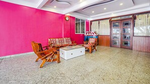 A room with a bright pink wall, wooden furniture, a white coffee table, and a large window with curtains. - Fabhotel Bns Lodge (Bengaluru)