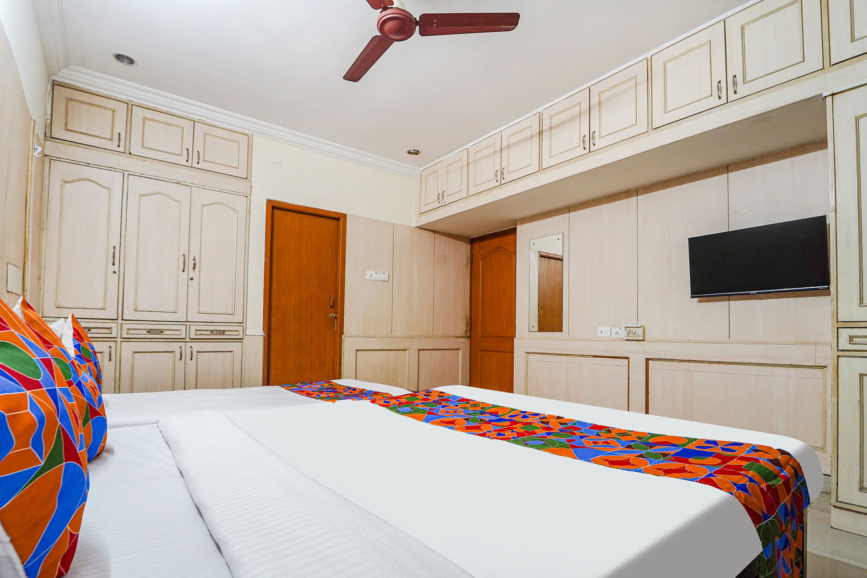 A hotel room with a bed, a ceiling fan, and a TV mounted on the wall.
