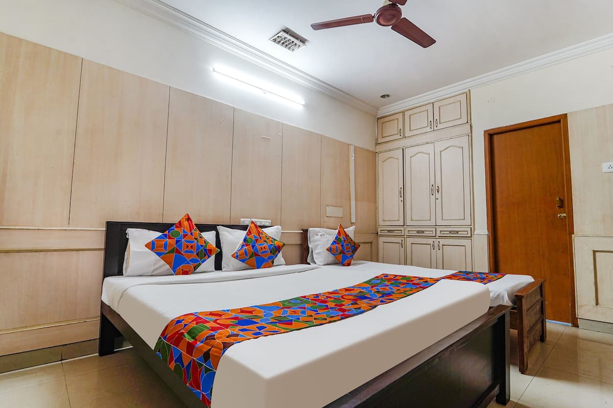 A hotel room with a large bed, wooden wardrobe, ceiling fan, and a door.