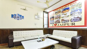 A hotel lobby with a white sofa set, a coffee table, and a wall with a poster advertising car taxis and Jaipur. - Fabhotel Sanjay Palace (Jaipur)