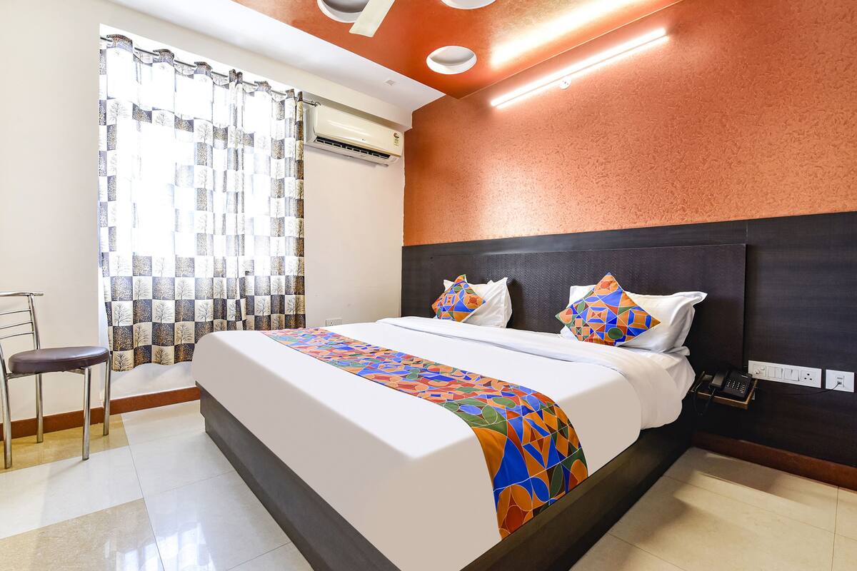 A hotel room with a large bed, a chair, a telephone, and an air conditioning unit.