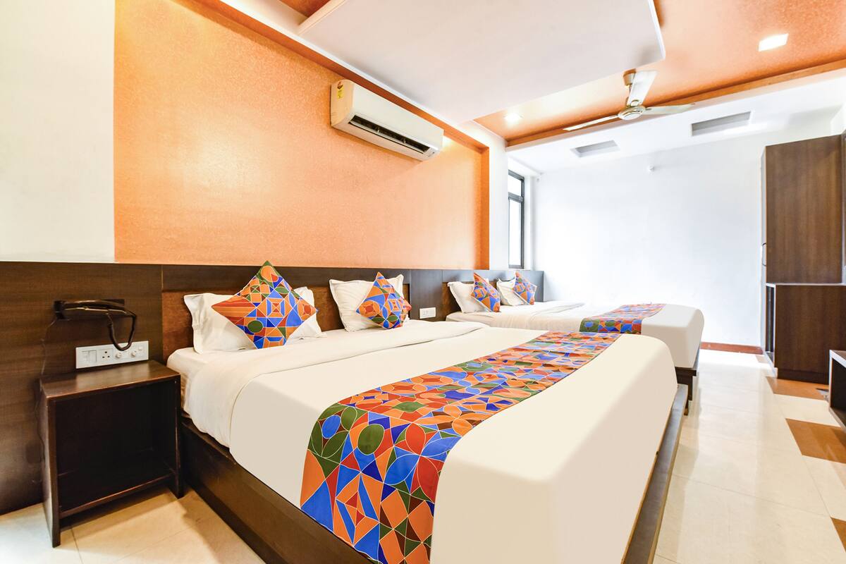 A hotel room with two beds, a nightstand, an air conditioning unit, and a wooden wardrobe.