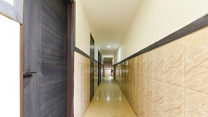 A long, narrow hallway with a dark wooden door on the left and a marble wall on the right. - Fabhotel Sanjay Palace (Jaipur)