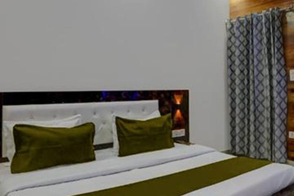 A modern hotel room with a large bed, green bedding, and a wooden accent wall.